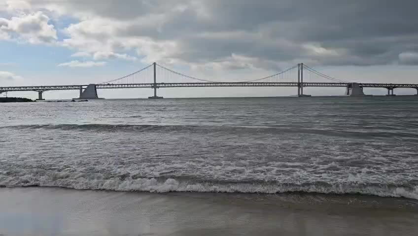 Close view of Gwangan Bridge from the shoreline with waves in the foreground, Busan