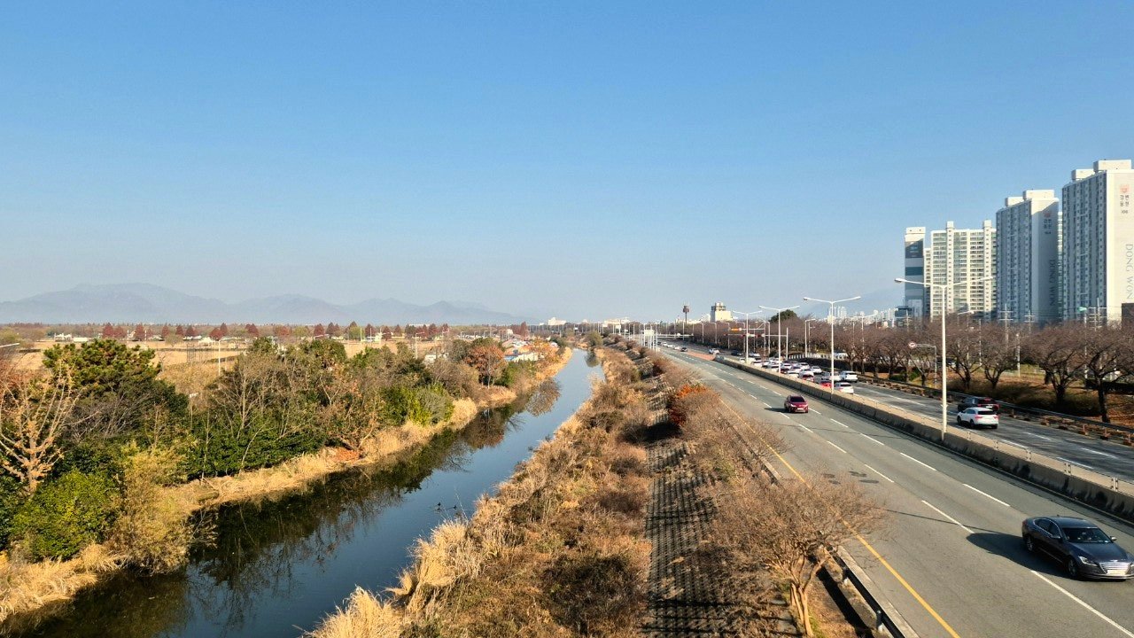 View along the Nakdong River levee road near Gupo, Busan, with distant mountains and apartment towers